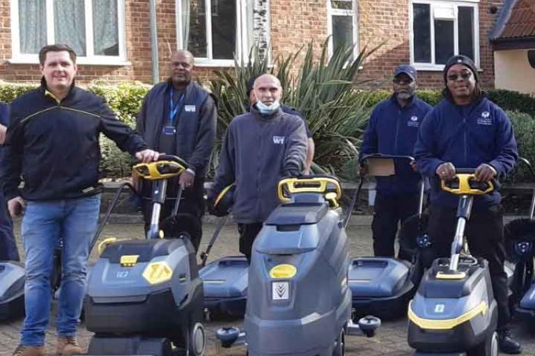 Five men and women standing in front of a house with street cleaning equipment.