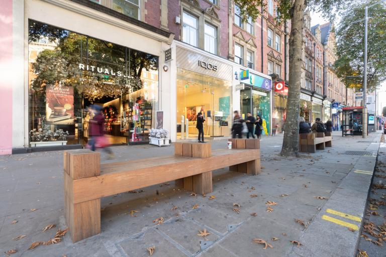 A high street row of shops with a wooden bench in front