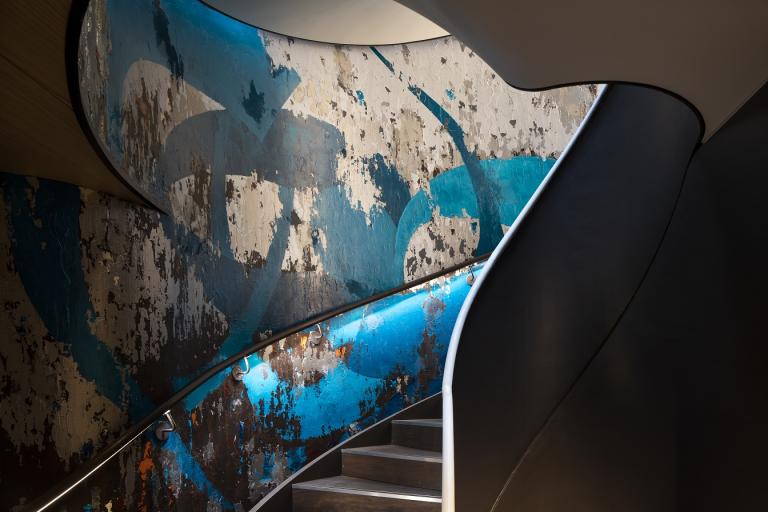 A curved staircase shows a blue and silver hand-painted mural lit 