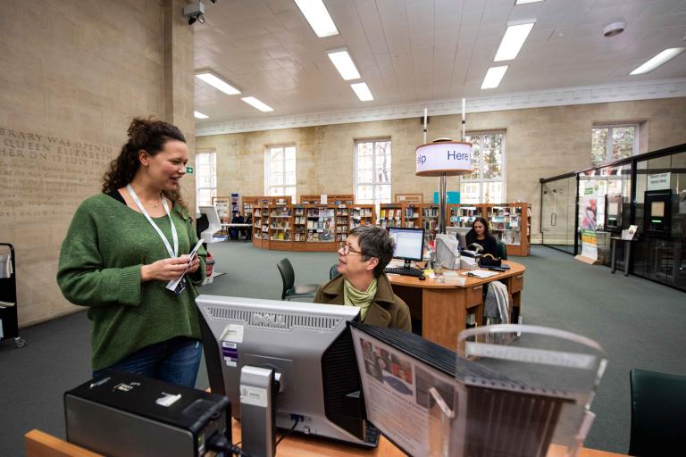 A female member of the libraries and archives team having a conversation with a female library customer.